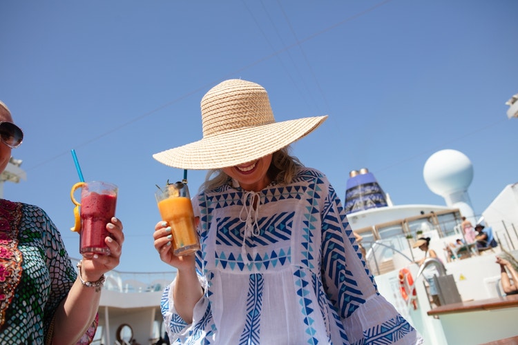 Two people in summer attire carry colorful smoothies on the Celestyal Discovery