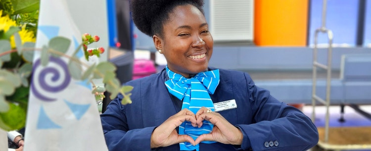 Celestyal crew member making a heart shape with her hands, smiling in her navy uniform.