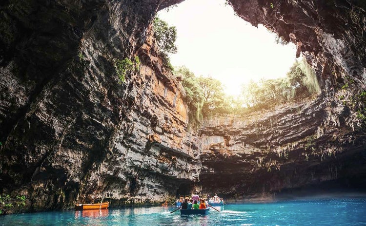Inside the Melissani Cave in Kefalonia, Greece, showing boats sailing on a crystal blue lake beneath a cavern with an open roof