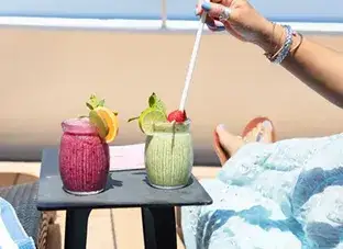A person places a white straw into a green smoothie, which is next to a pink smoothie on a table