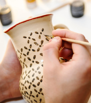 A person paints a pattern on a ceramic jug