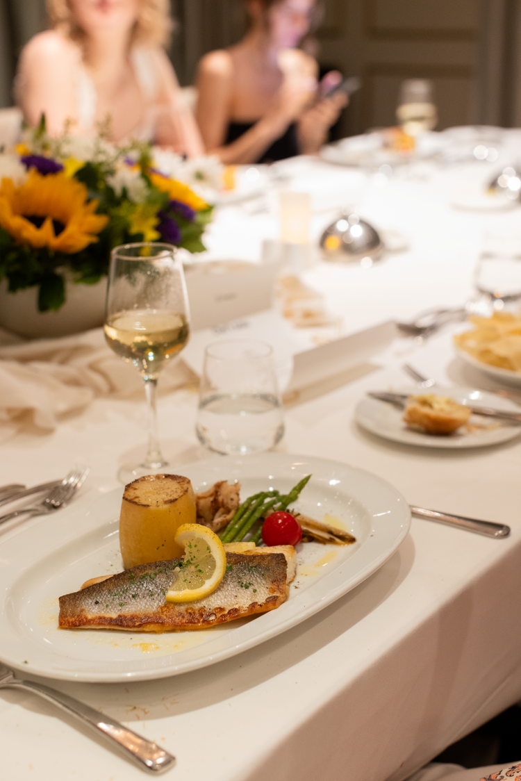 A glass of white wine and a plate of fish and vegetables on a table