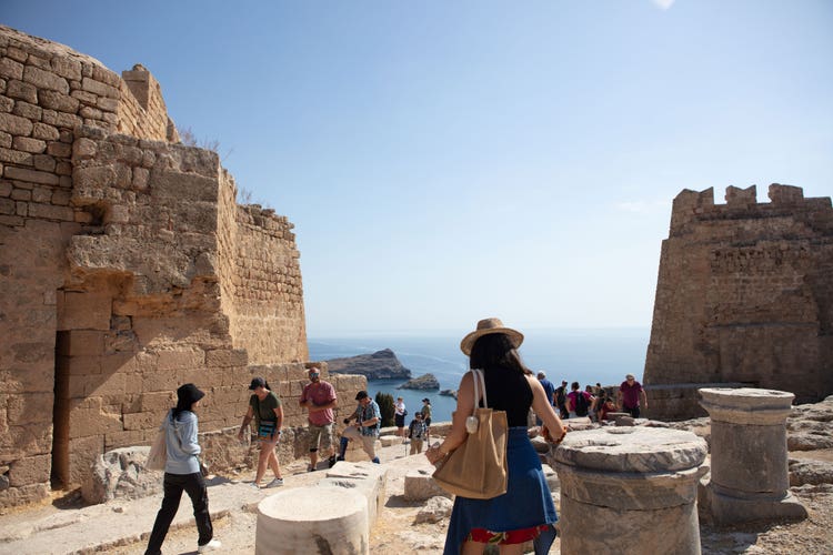 Tourists exploring ancient hilltop ruins overlooking the sea in Greece.