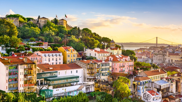 Aerial view of colourful Mediterranean village houses with terracotta rooftops perched dramatically on a rocky coastal outcrop, surrounded by vivid crystal-clear turquoise waters — discover iconic Greek island destinations with Celestyal Cruises. Overlaid with messaging that says &#34;Save up to 60% off 2026/27 Mediterranean cruises