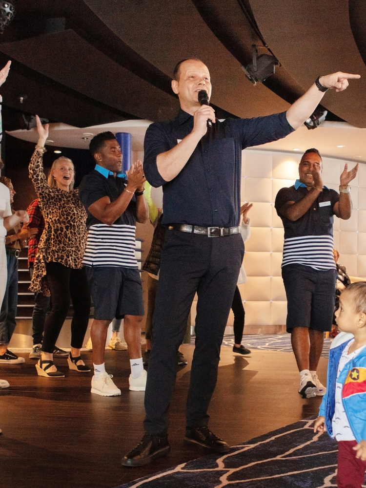 A member of the Celestyal Discovery crew holds a microphone and entertains passengers