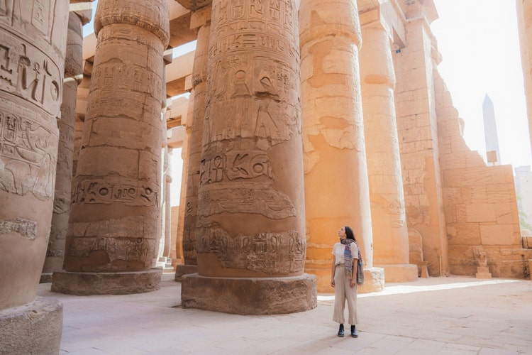 photograph of a woman stood in front of hieroglyphed pillars at the Temple of Karnak, Egypt