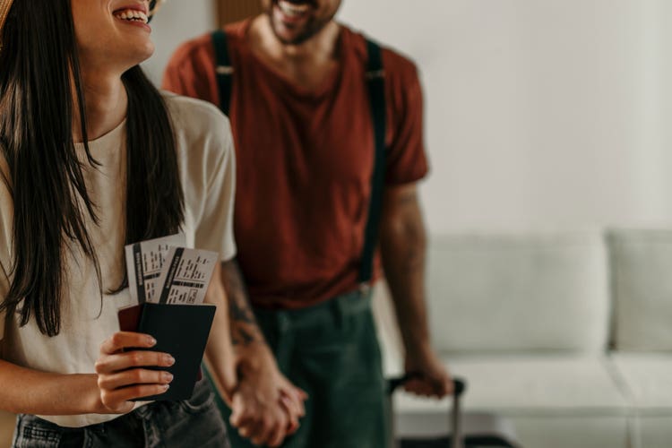 Smiling couple holding passports and boarding passes while travelling with luggage.