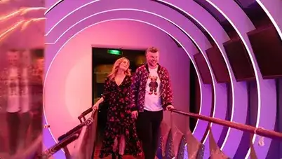 Two people walk down the neon-lit tunnel of the Celestyal Discovery’s AFTer Disco Bar &amp; Lounge